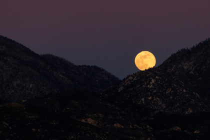 Une pleine lune, orange à cause de la fumée de l'incendie d'Eaton, se lève au-dessus des montagnes de la forêt nationale d'Angeles au nord d'Altadena, en Californie, le 13 janvier 2025