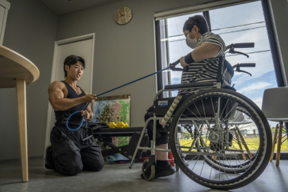 Hokuto Tatsumi (g), auxiliaire de vie et culturiste, aide une patiente (d) à s'entraîner dans un foyer pour personnes handicapées géré par Visionary à Ichinomiya, au Japon, le 29 septembre 2025 - Yuichi YAMAZAKI (AFP)