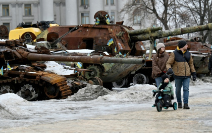 Un couple et un enfant à vélo se promènent dans l'exposition en plein air d'équipements militaires russes détruits à Kiev, le 15 février 2026 - Sergei SUPINSKY (AFP)