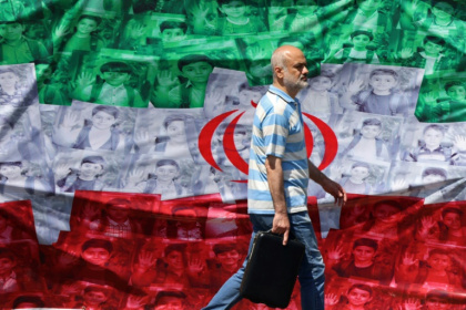Un homme passe devant un drapeau iranien installé le long de la route à Téhéran le 29 avril 2026 - ATTA KENARE (AFP)