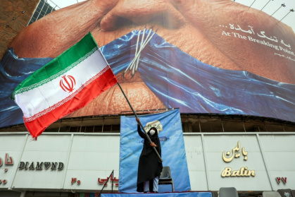 Une femme agite un drapeau iranien devant une affichage anti-américaine faisant référence au président américain Donald Trump et au détroit d'Ormuz à Téhéran, le 5 mai 2026 - Photographe inconnu (AFP)