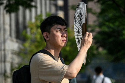 Un homme se protège du soleil avec un éventail, le 13 juillet 2026 à Séoul - JADE GAO (AFP)
